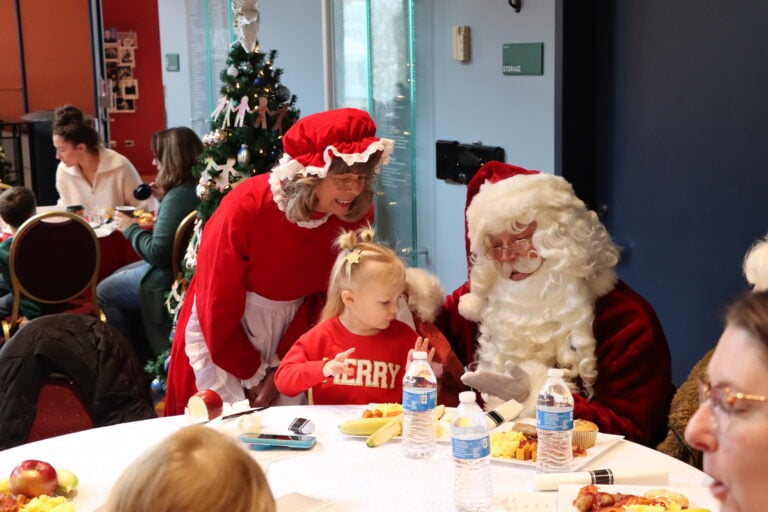 A small child eats breakfast with Santa and Mrs. Claus during Breakfast With Santa at Whitaker Center in 2024.